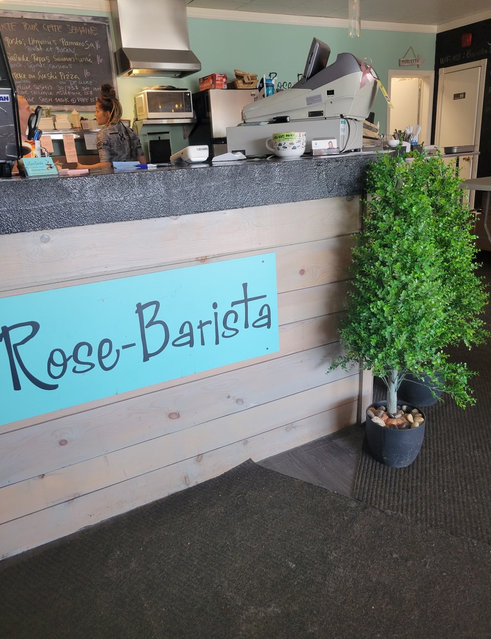 L'enseigne « Rose-Barista » peinte sur un mur de planches blanches, près du comptoir